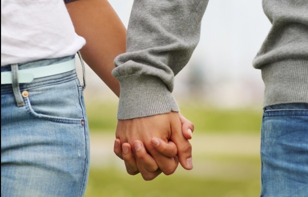 Mid section closeup image of a young couple holding hands, outdoors